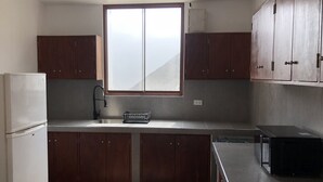A kitchen with wooden cabinets, a window, a refrigerator, and a microwave.