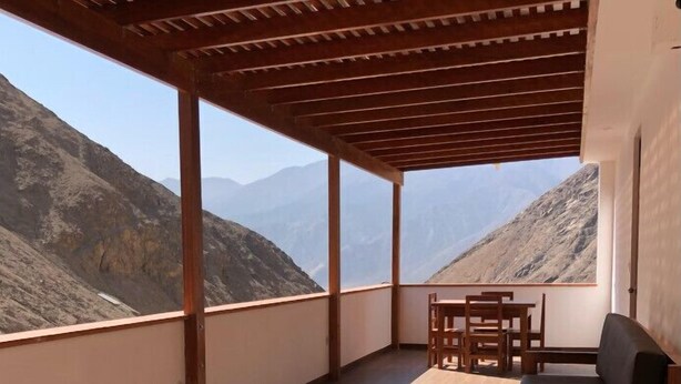 A balcony with a wooden pergola, a sofa, and a table with chairs.