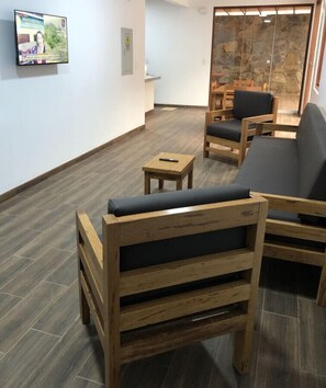 Une pièce meublée de meubles en bois, notamment un canapé et des fauteuils, une petite table et un téléviseur fixé au mur.