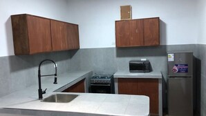 A compact kitchen with a stainless steel sink, a gas stove, a microwave, and a refrigerator. - Spacious 3-bedroom and 2 bathroom home with private pool and patio and free Wi-Fi (Calango)