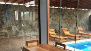 A wooden dining table with chairs in a room with a stone wall and a glass door leading to a pool area. - Spacious 3-bedroom and 2 bathroom home with private pool and patio and free Wi-Fi (Calango)