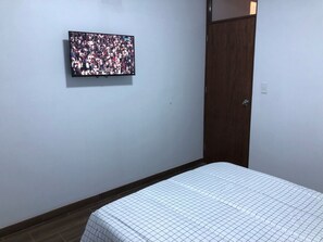 A room with a bed, a television mounted on the wall, and a wooden door.