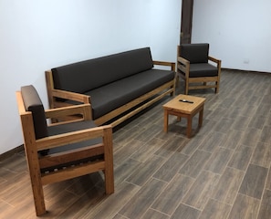 A room with a dark grey sofa, two wooden chairs, and a small wooden table.