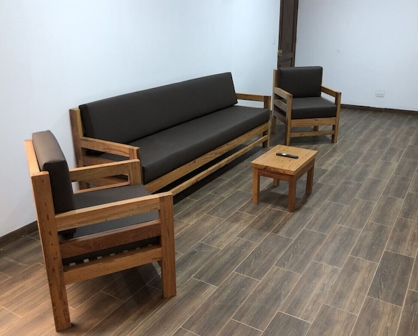 Une pièce avec un canapé gris foncé, deux chaises en bois et une petite table en bois.