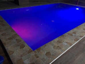 En swimmingpool med en blå spejlen­de overflade og stenfliser rundt langs kanten.