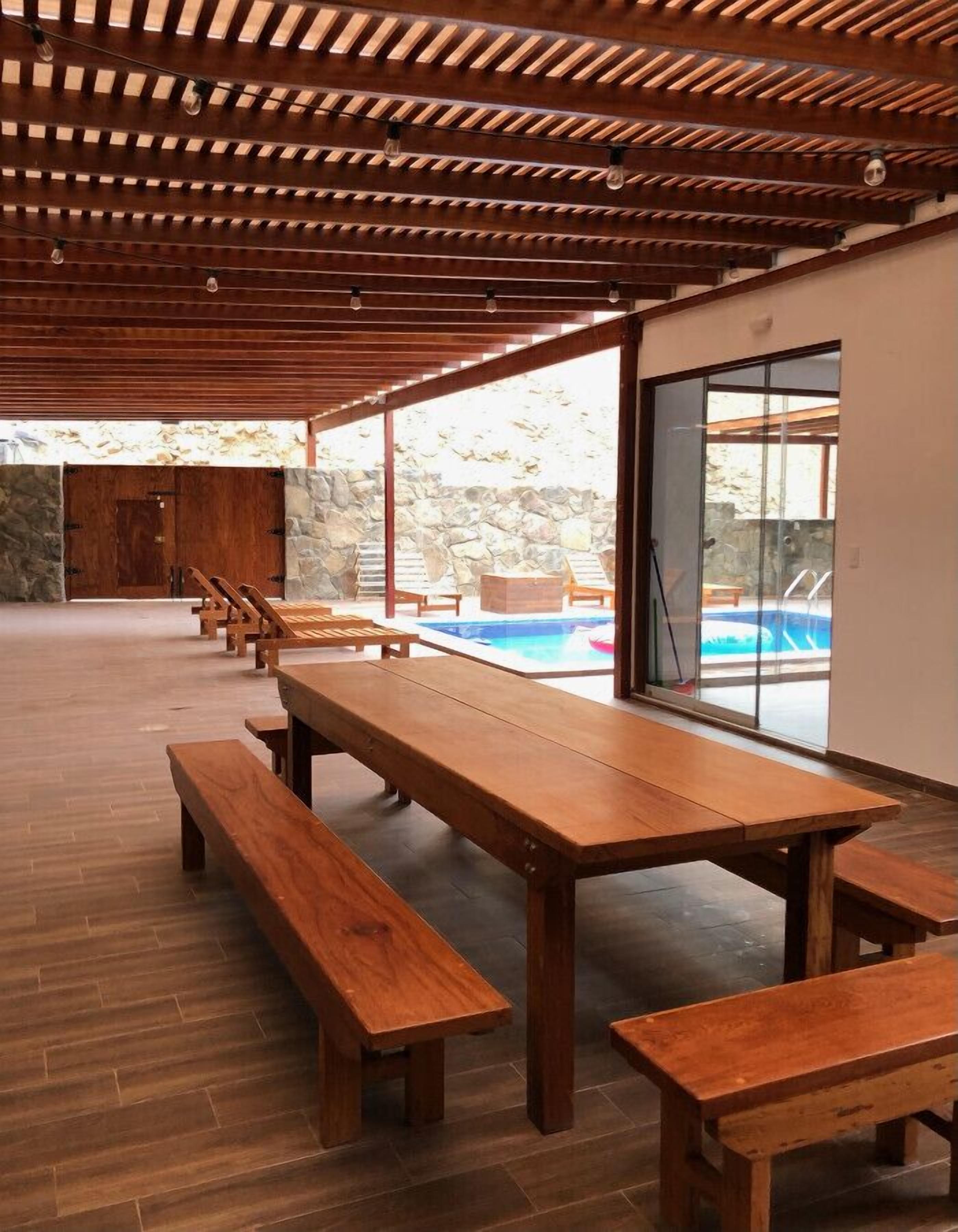 Un espace extérieur abrité, doté de bancs et de tables en bois, d’un mur en pierre et offrant une vue sur une piscine.