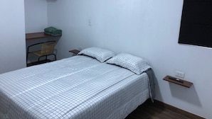 A small, neatly arranged bedroom with a single bed, a chair, a shelf with a green towel, and a wall-mounted TV. - Spacious 3-bedroom and 2 bathroom home with private pool and patio and free Wi-Fi (Calango)