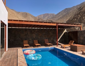 Una piscina con tumbonas de madera y un muro de piedra de fondo.