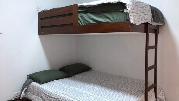 Un letto a castello con una scala, un letto singolo in basso e un cuscino verde.