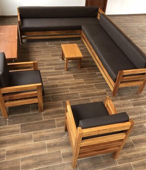 Un canapé modulable, deux chaises en bois et une petite table en bois, le tout dans une pièce dont le sol est recouvert de parquet.