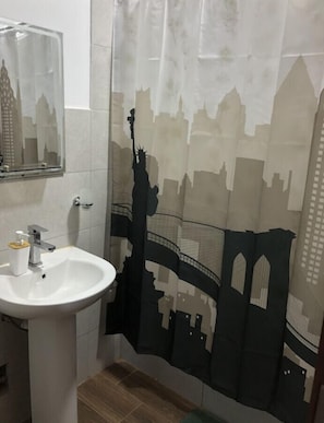 Un baño con lavabo blanco, un espejo y una cortina de ducha con el dibujo de un horizonte urbano.