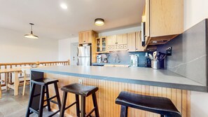 A modern kitchen with wooden cabinets, a large island with stools, stainless steel appliances, and pendant lighting.