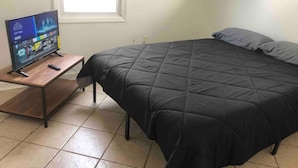 Un dormitorio con una cama, un televisor sobre un soporte de madera y una ventana.