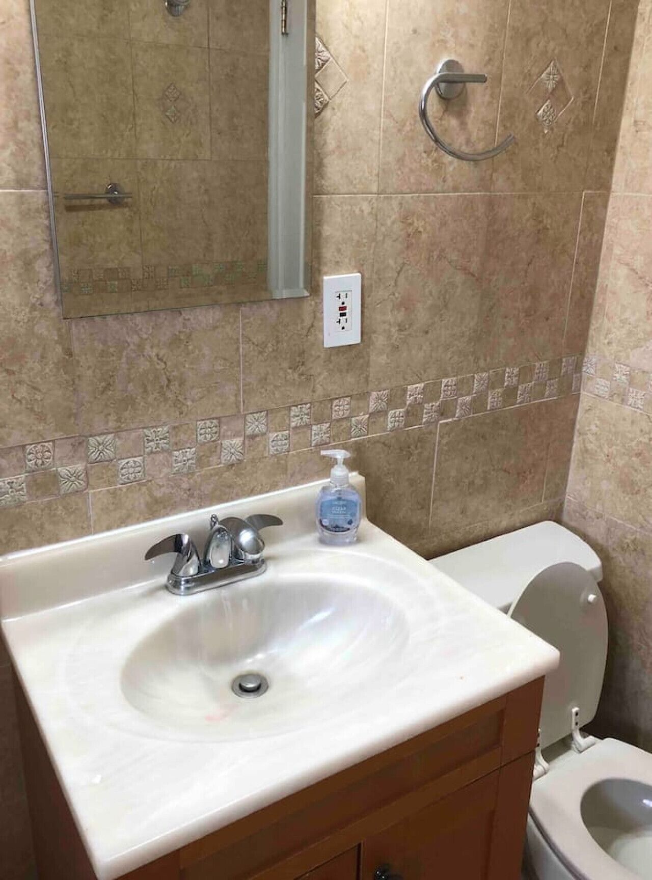 A bathroom with a white sink, a mirror, a toilet, and a wall-mounted electrical outlet.
