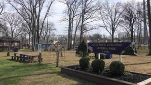 Un parque con un monumento conmemorativo dedicado al alcalde Frank G. Pelzman, mesas de picnic y árboles sin hojas.