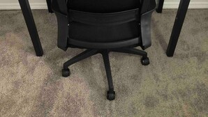 Una silla de oficina negra con respaldo de malla y ruedas, sobre un piso alfombrado.