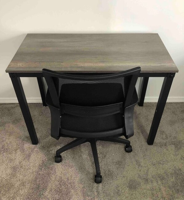 A black office chair with a mesh backrest and wheels, positioned on a carpeted floor.
