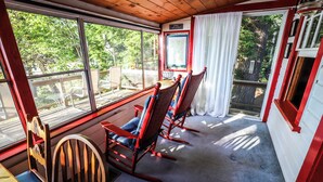 Una habitación con vistas al exterior, sillones mecedores, una mesa y una ventana con cortinas.