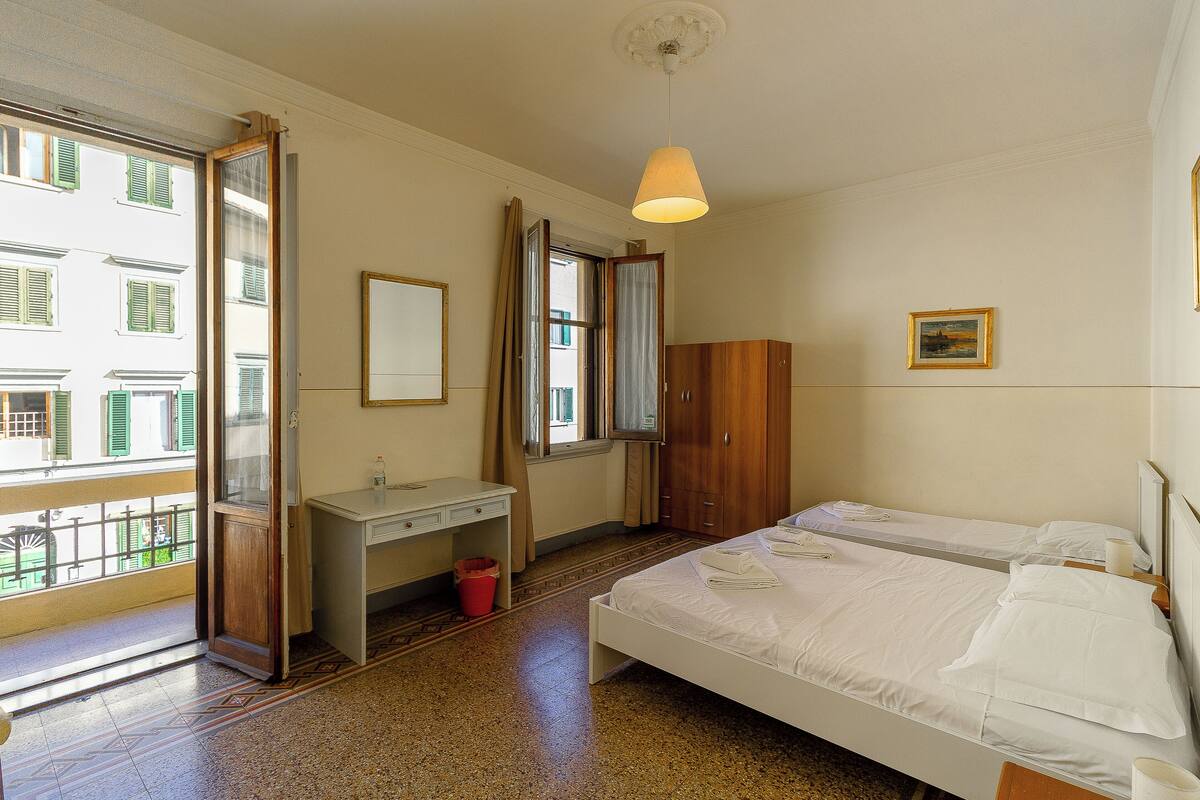 Habitación de hotel con cama, escritorio, armario, ventana con cortinas y un cuadro en la pared.