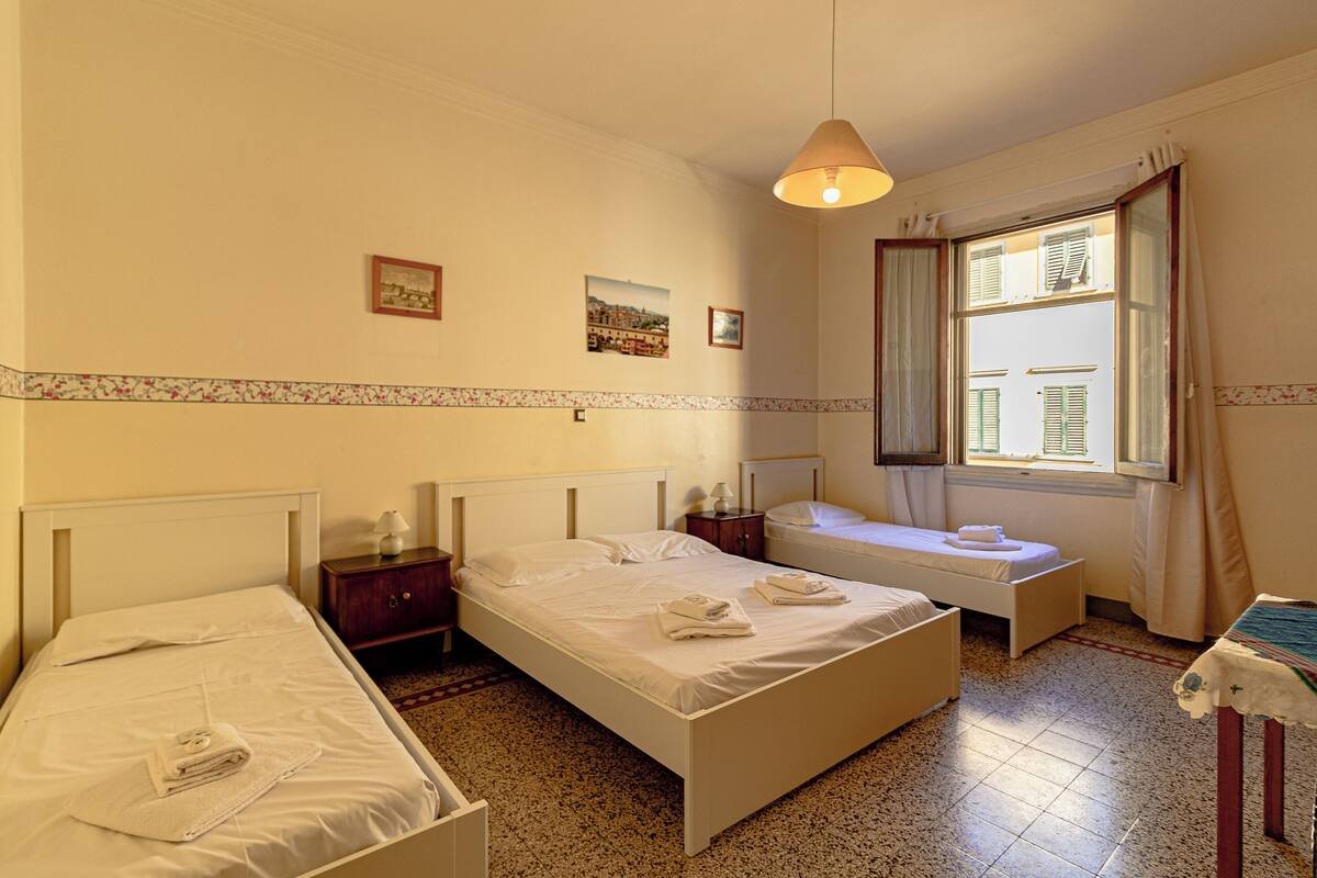 Una habitación de hotel con dos camas individuales, una mesita, un banco y una ventana con cortinas.