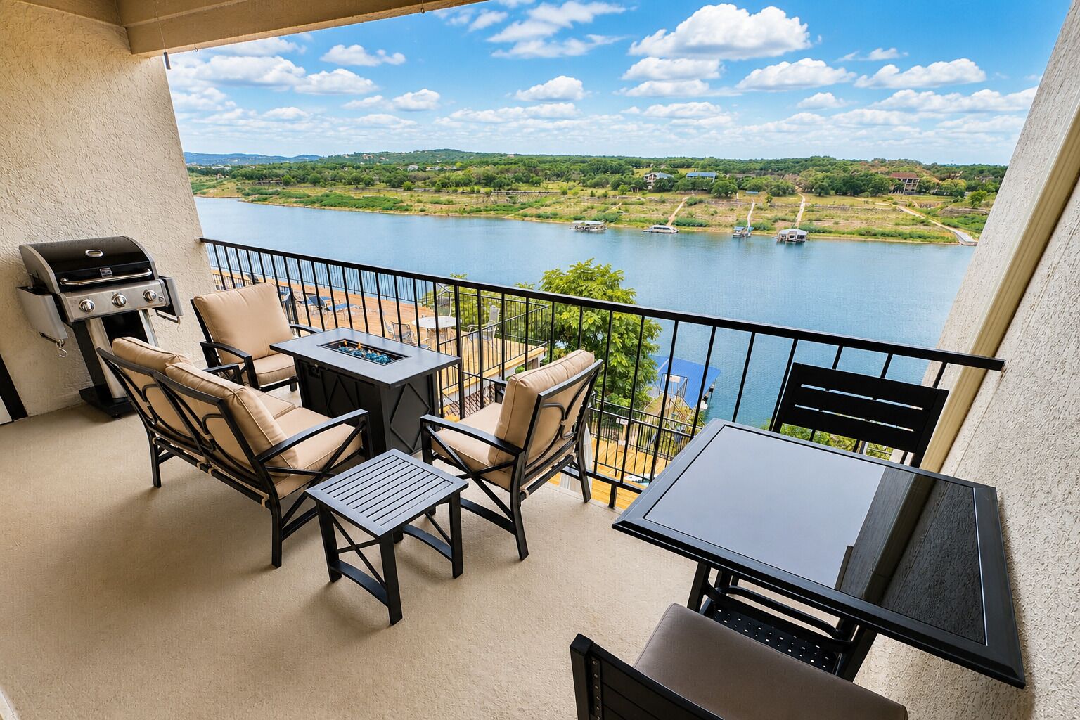 A balcony with outdoor furniture, a grill, and a view of a lake and distant landscape.