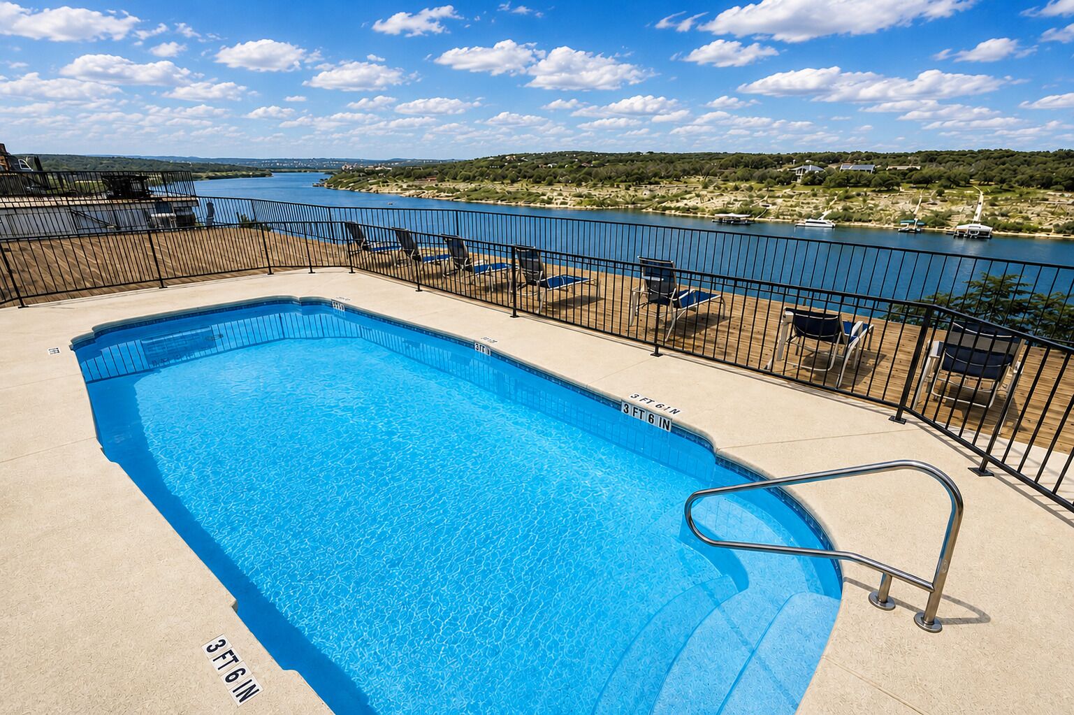 Piscina rectangular con barandilla de seguridad metálica, rodeada de sillas de descanso y vista a un lago y paisaje distante.