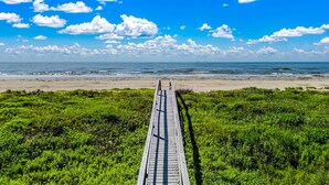 A wooden boardwalk leading to a beach with a clear sky and scattered clouds.