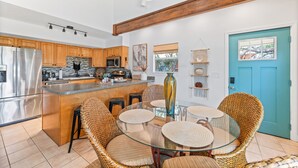 A modern kitchen with wooden cabinets, a stainless steel refrigerator, a central island with bar stools, and a blue door.