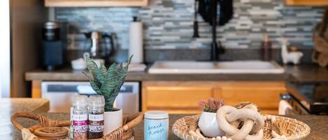 A kitchen counter with a coffee maker, a plant, a jar labeled 'beach house', and a basket with pretzels and a woven item.