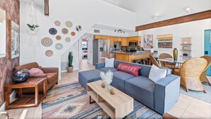 A spacious living area with a sofa, coffee table, and a dining table with chairs. A kitchen is visible in the background.