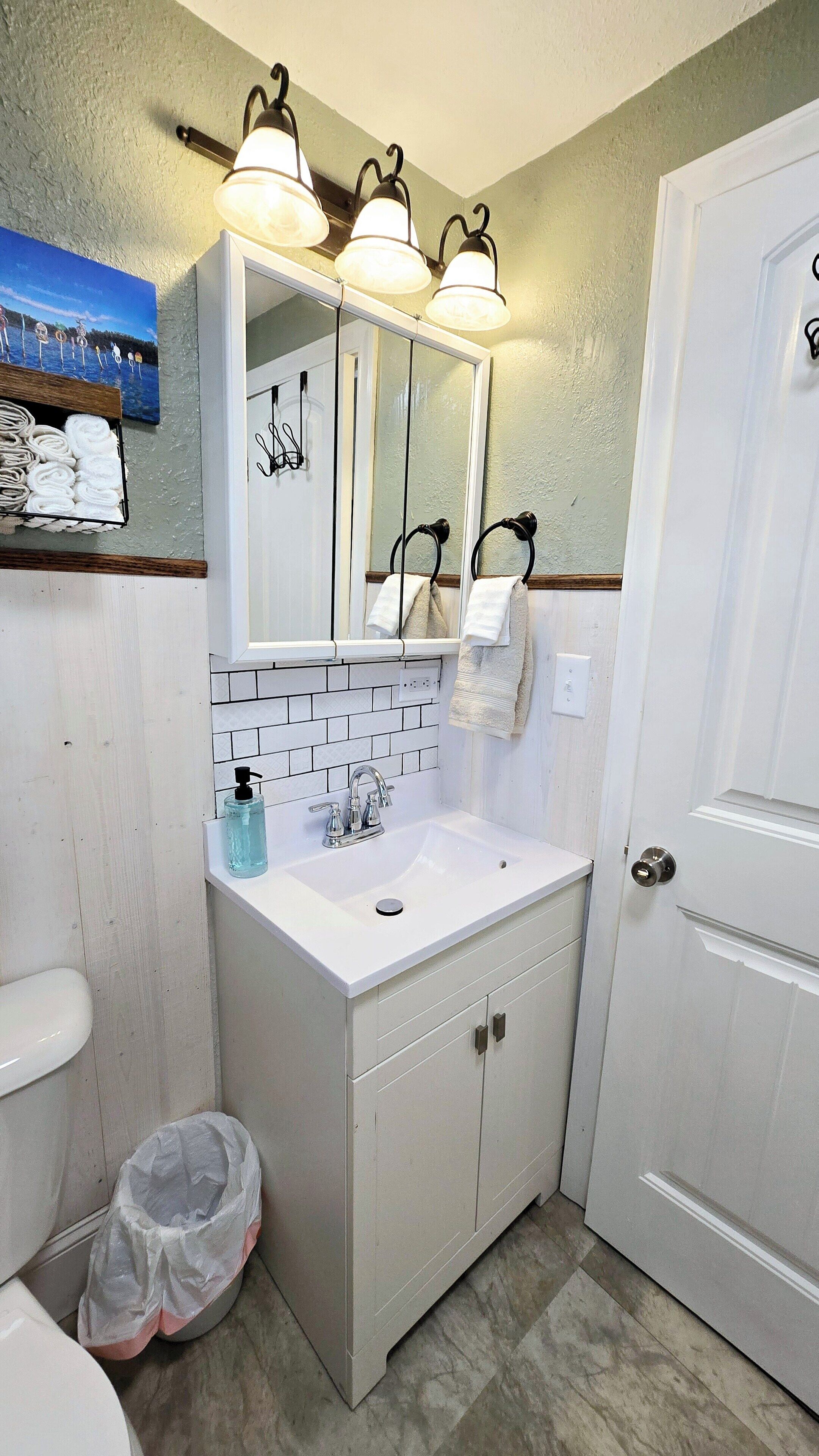 Une salle de bain avec un lavabo blanc, un miroir et trois appliques murales.