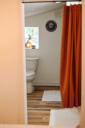 Une salle de bain avec des toilettes, une fenêtre avec une plante et un autocollant mural.