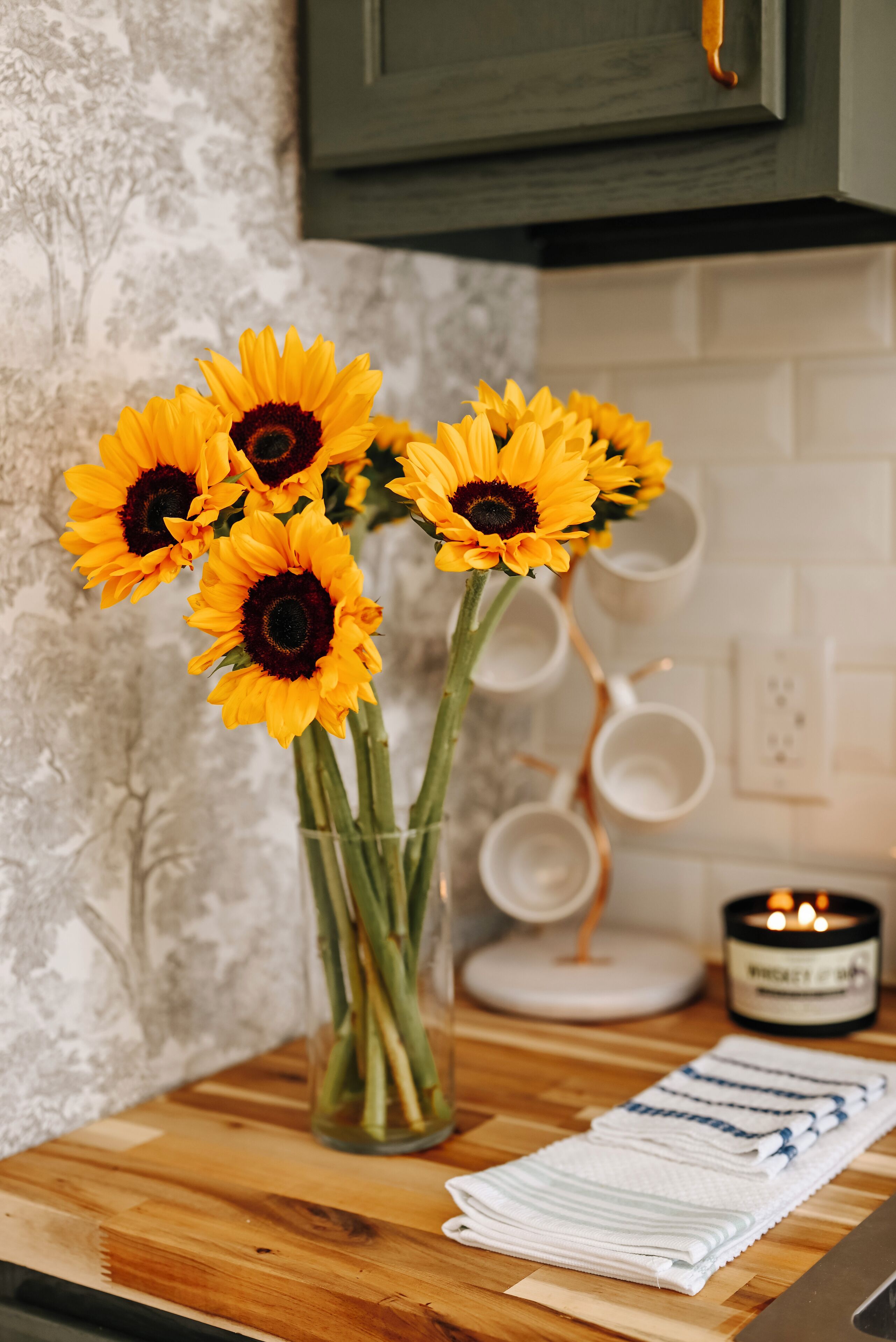 Un comptoir de cuisine orné d’un vase de tournesols, d’une bougie et d’un ensemble de tasses blanches.