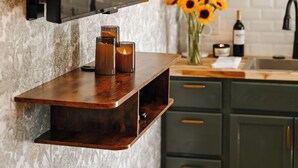 A kitchen with a built-in wooden shelf, a wall-mounted TV, and a vase with sunflowers.