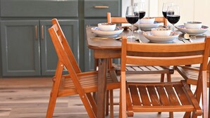 A wooden dining table set with plates, bowls, and wine glasses, with a kitchen in the background.