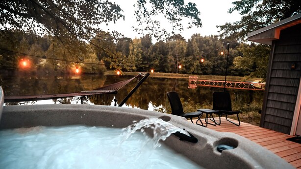 A hot tub with a wooden deck, surrounded by trees and a wooden structure.
