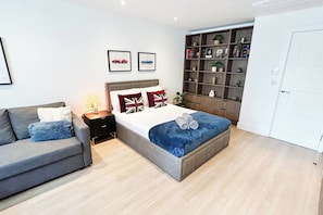 A modern bedroom with a bed, a sofa, a nightstand, a bookshelf, and a wardrobe.