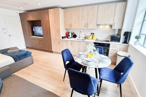 A modern kitchen with wooden cabinets, a dining table set for four, and a television in the background.
