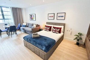 Una habitación de hotel moderna con cama, sofá, mesa de comedor y sillas. Hay cuadros enmarcados en la pared.