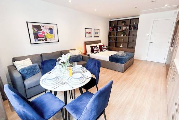 A modern living room with a sofa, a dining table set for four, and a bookshelf.