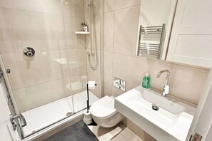 Un baño moderno con ducha envuelta en cristal, inodoro, lavamanos con espejo y un perchero para toallas.