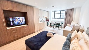 Habitació d'hotel moderna amb un televisor gran, un sofà, zona de menjador i cuina.