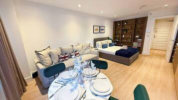 A modern living room with a dining area set for a meal, a sofa with pillows, a bookshelf, and a door leading to another room.