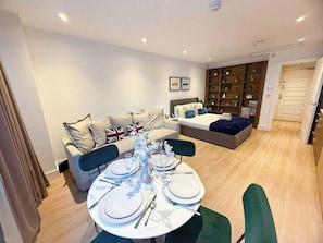 Una sala de estar moderna con comedor listo para una comida, un sofá con almohadas, una estantería y una puerta que da a otra habitación.