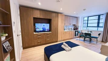 A modern hotel room with a bed, a TV, a kitchenette, and a dining area.