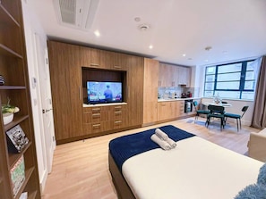 Una habitación de hotel moderna con cama, televisor, kitchenette y comedor.