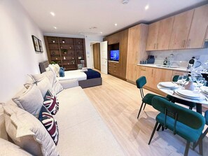 Una sala de estar moderna con un sofá, un comedor con una mesa lista para dos personas y una cocina con armarios de madera y un televisor.