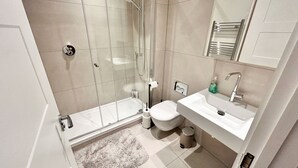 Un bany modern amb una dutxa tancada amb vidre, un vàter i un lavabo amb un mirall a sobre.