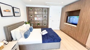 Un dormitori modern amb un llit, una televisió, una prestatgeria i una porta.