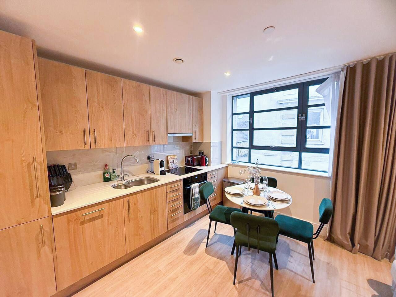 A modern kitchen with wooden cabinets, a dining table with chairs, and a window with curtains.